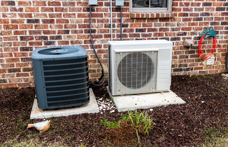 Air Conditioner unit and heat pump located at the side of a brick home.